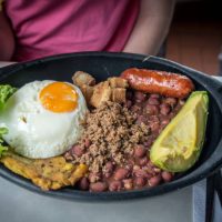 A traditional dish from Colombia - Bandeja Paisa, includes ground beef, chorizo sausage, greaves, red beans, fried egg, avocado and plantain